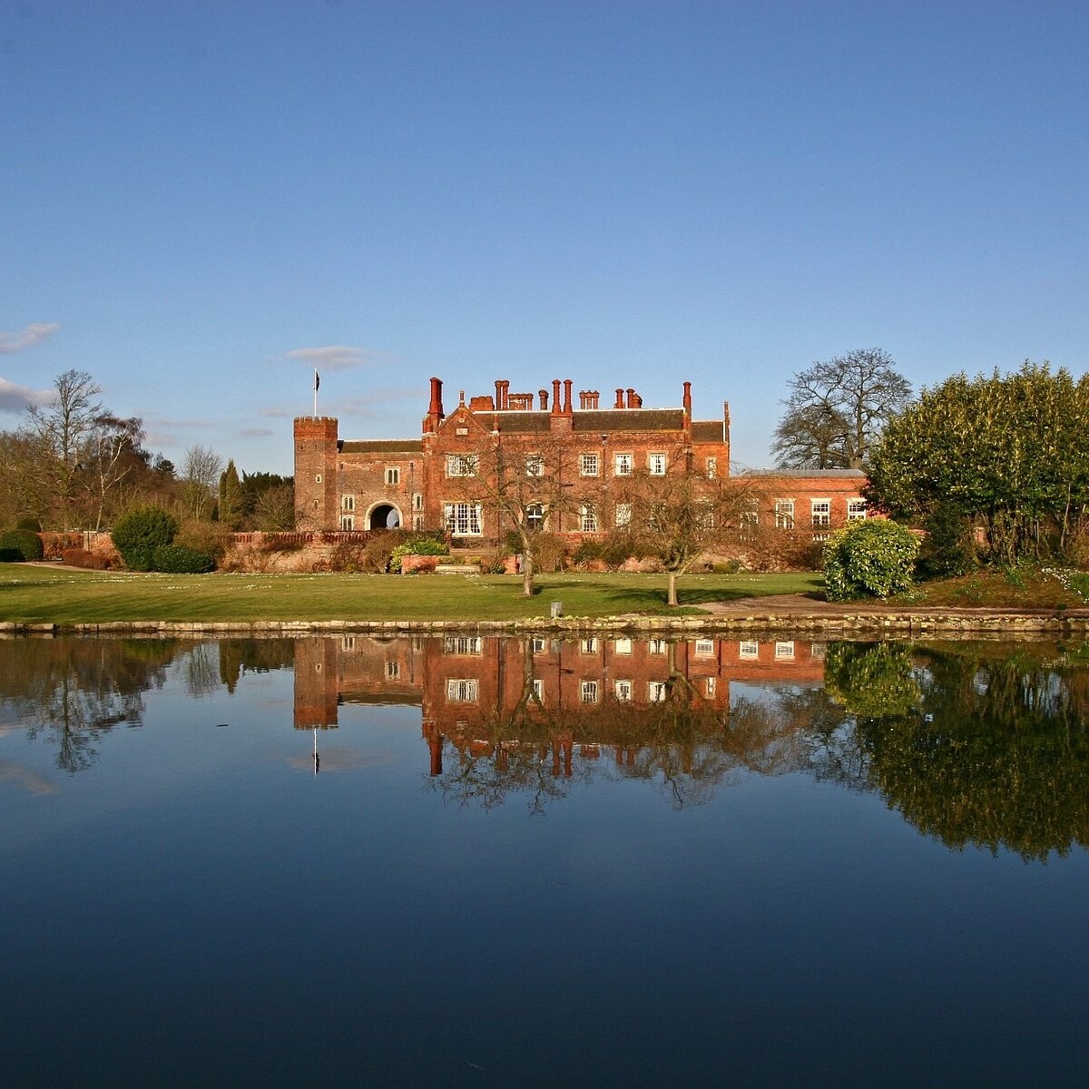 Hodsock Priory in Nottinghamshire viewed across a lake, with the historic red-brick house reflected in calm water and gardens.