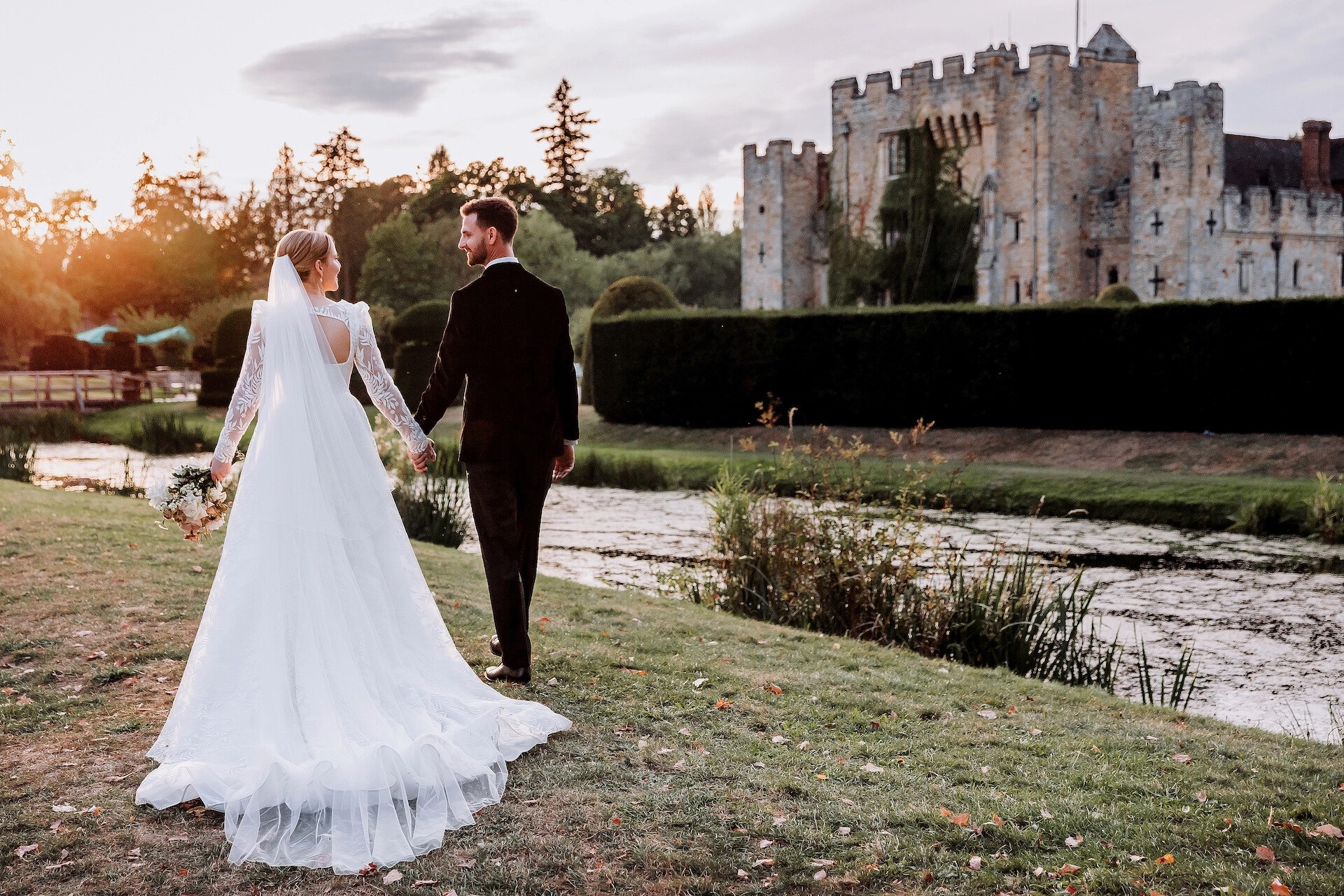Couple walking past gardens and exterior of Hever Castle and Gardens wedding venue