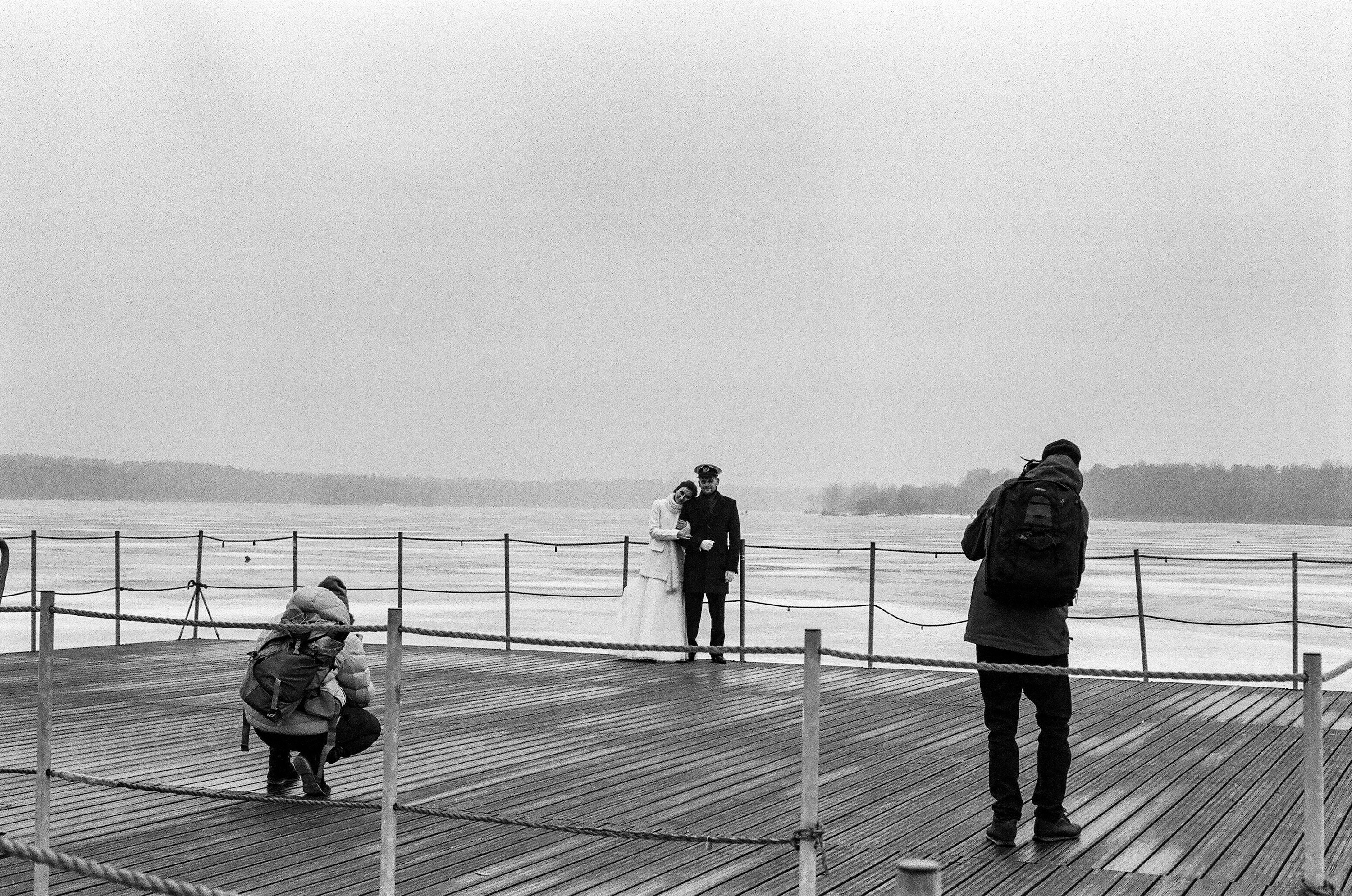 Wedding couple photoshoot on a seaside pier, with two photographers capturing the moment from different angles.