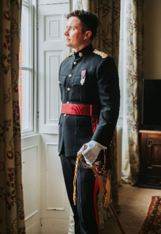 Groom in military uniform holding a sword, looking out the window