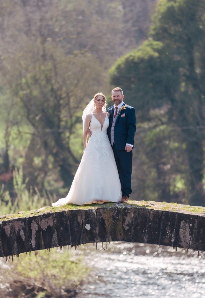 bride and groom stood on a bridge over a river at Shireburn Arms 