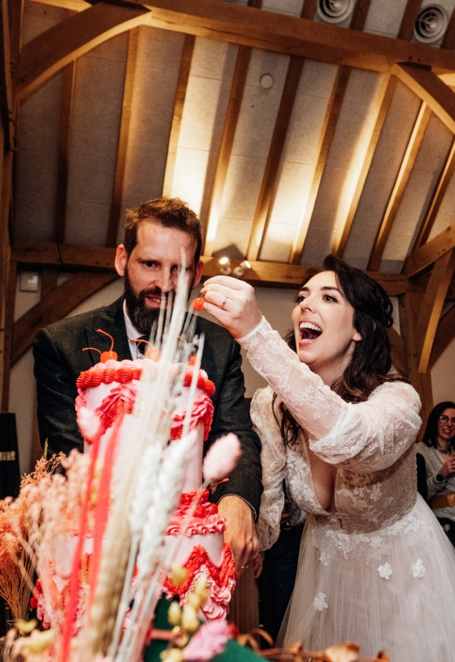 Bride eats a cherry from the top of her pink and red wedding cake