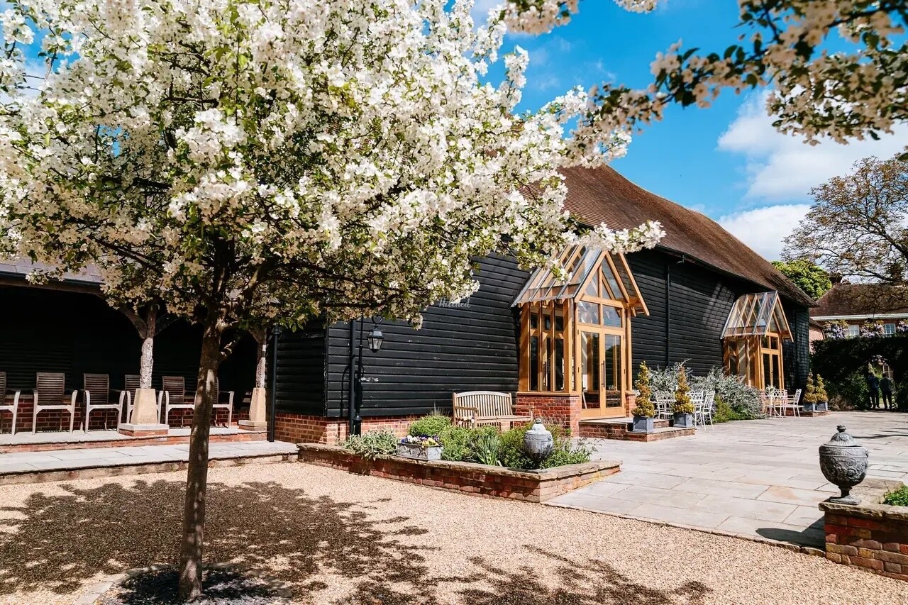 Exterior of Micklefield Hall with a barn-style building, courtyard seating and blossom trees in the gardens