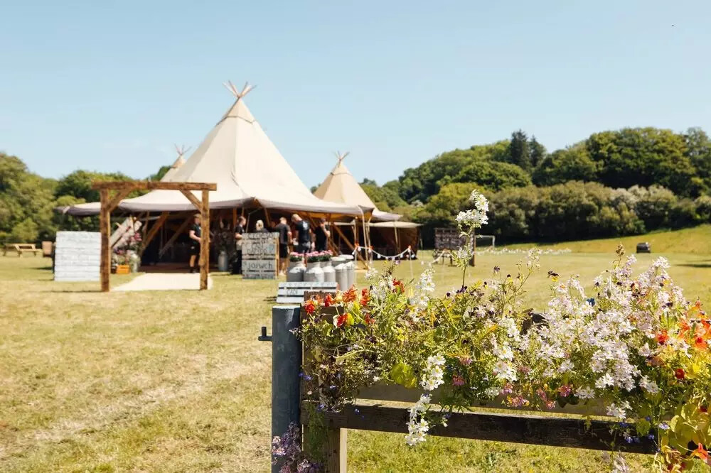 Outdoor wedding tipis in a countryside field with floral displays by JAVA Tipis Ltd.