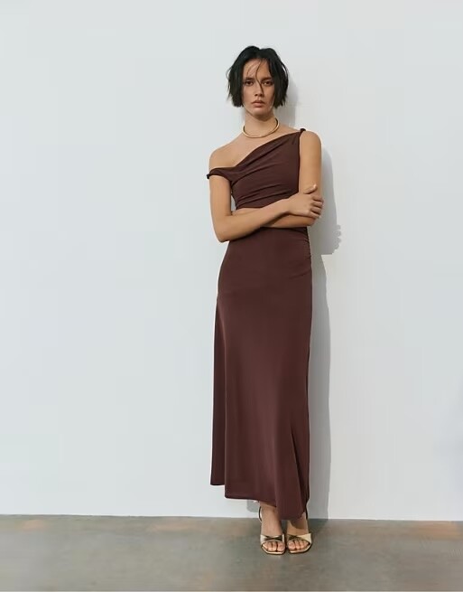 Model wearing a chocolate brown one-shoulder satin bridesmaid dress with draped neckline and midi length skirt.