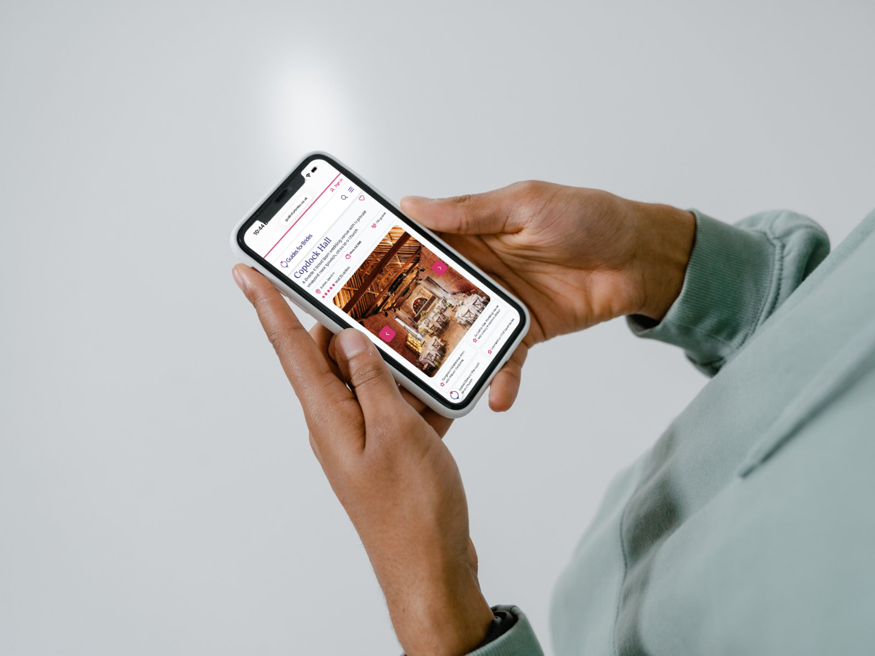 User holds a phone which shows the Guides for Brides wedding directory listing of a venue on screen.