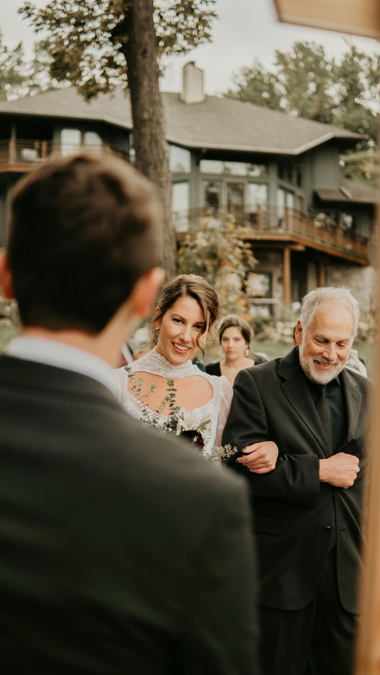 Bride walking arm in arm with her father towards her partner at an outdoor wedding ceremony