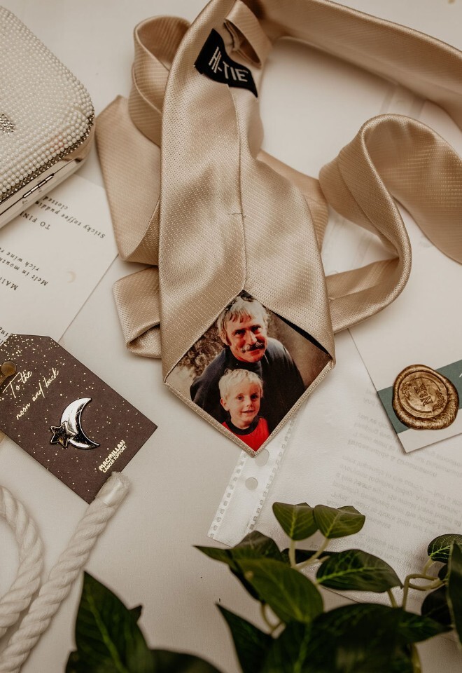 Flat lay of wedding details including groom’s tie, personalised photo detail, handfasting cord, stationery and bride’s beaded purse.