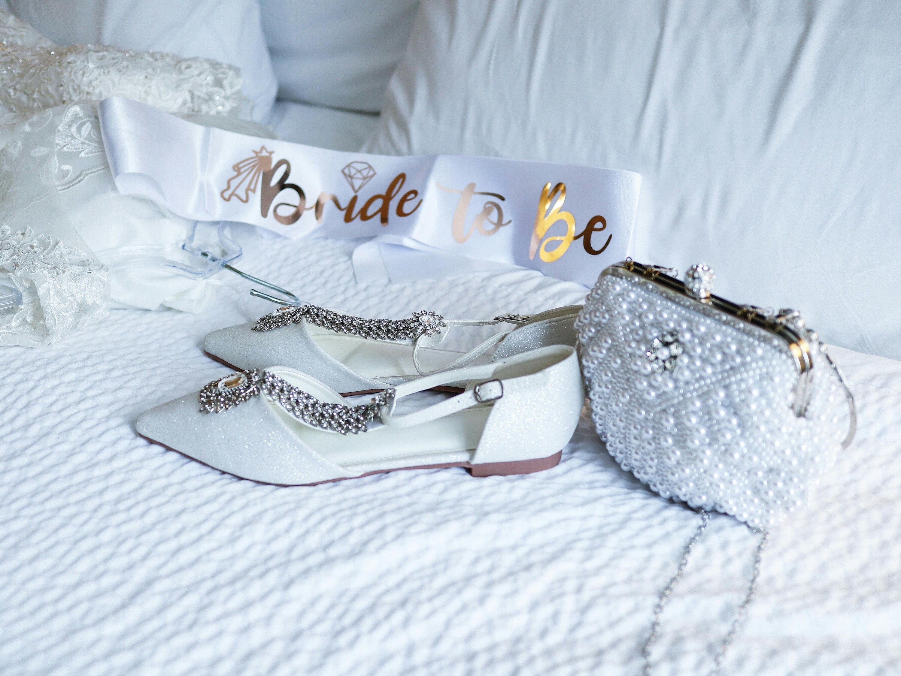 Bridal accessories, including white bridal shoes, a pearl clutch bag and a bride to be sash