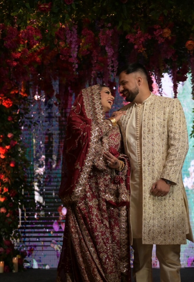 Bride and Groom staring into each others eyes romantically and laughing under the beautifully decorated floral arch