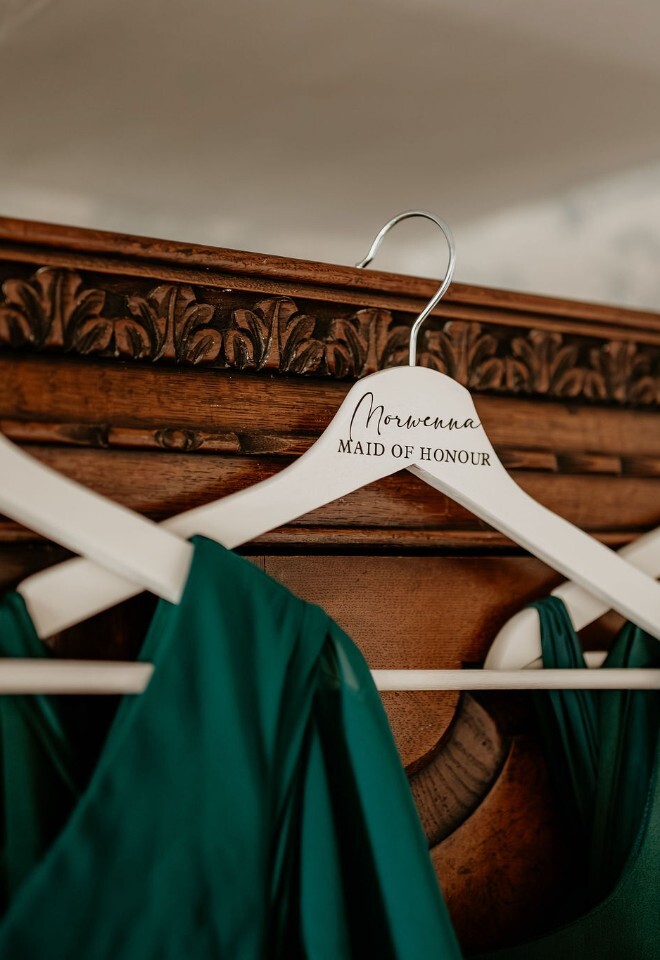  green bridesmaid dresses hung up on white personalised hangers with names in wedding dressing room. 