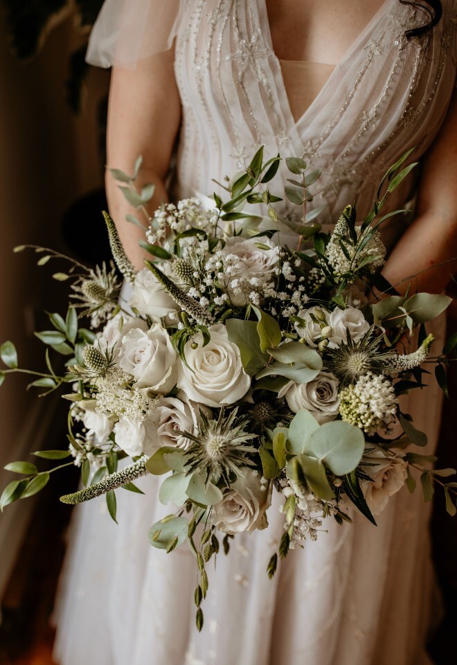 Bride holding a white roses and green bouquet against a detailed wedding dress.