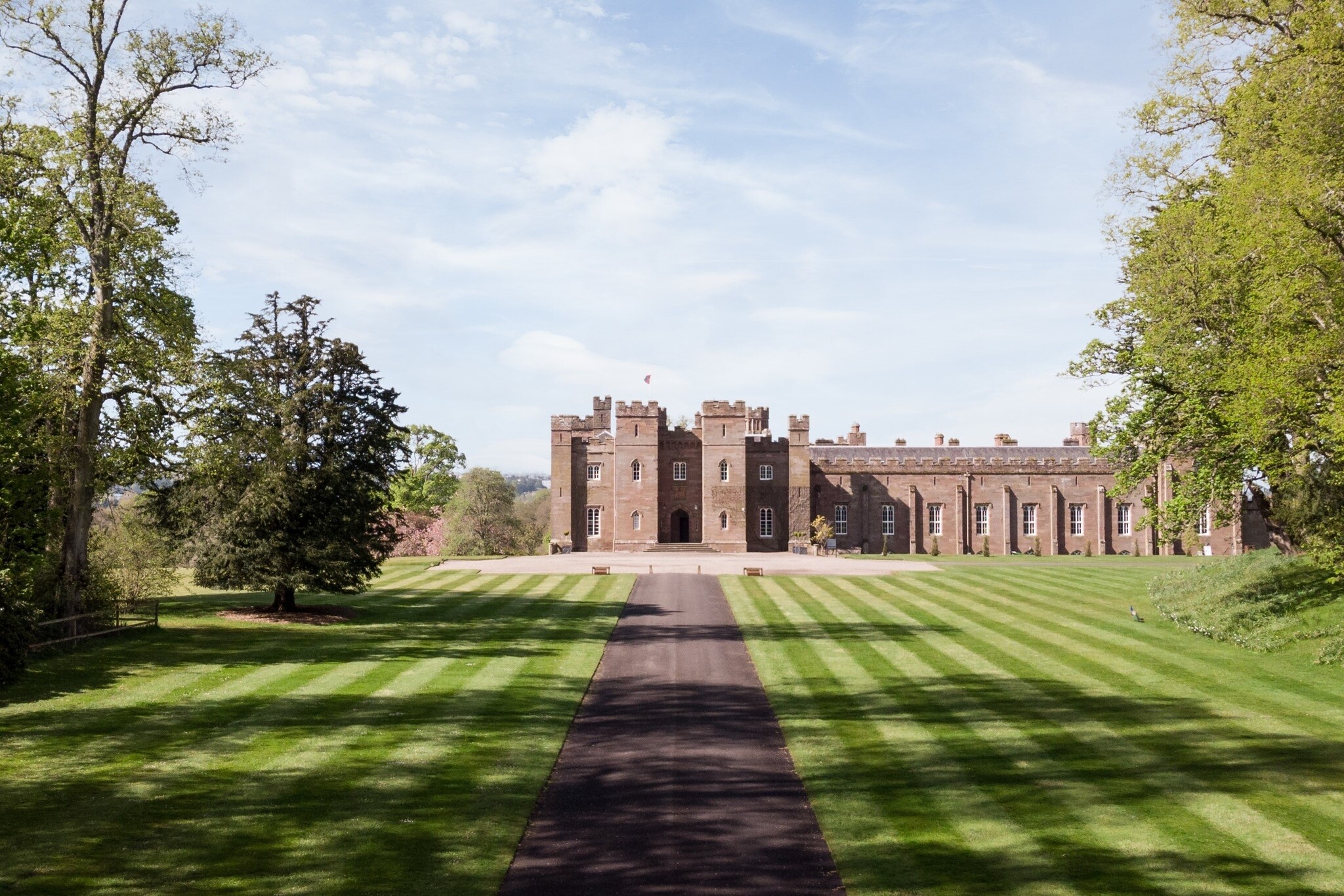 A long driveway heading towards Scone Palace in Scotland. The facade of the venue can be seen at the end of the road.