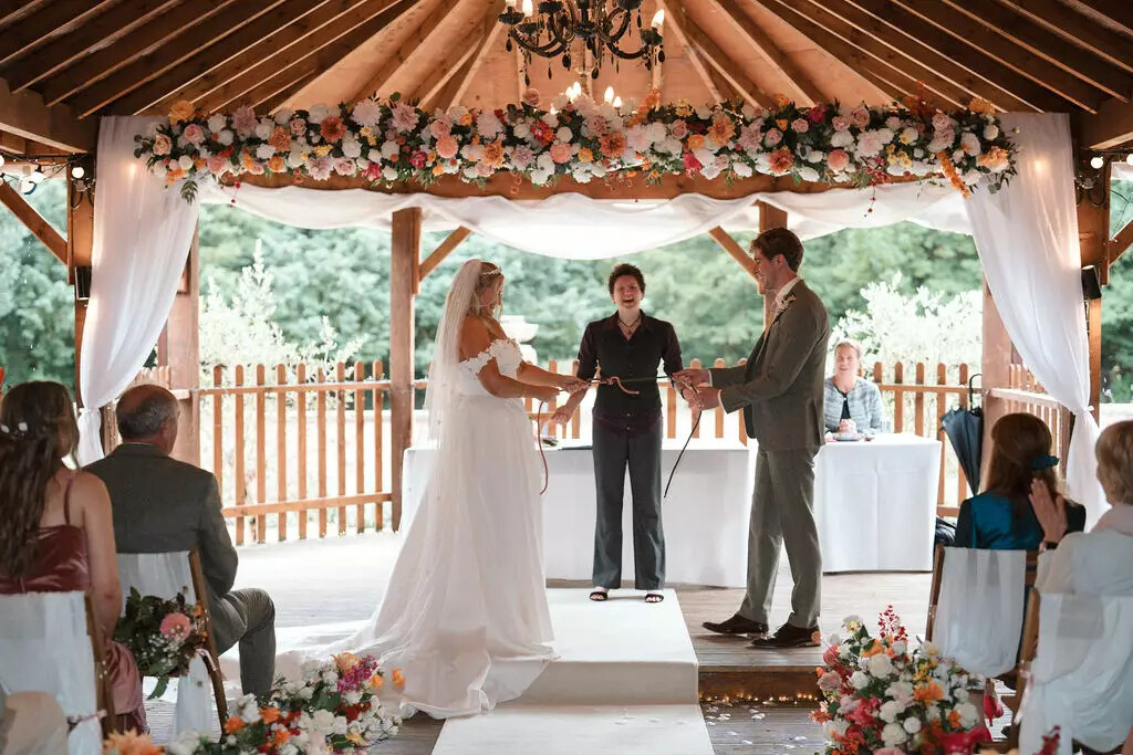 Bride and groom taking part in handfasting ceremony surrounded by warm autumn colour flowers