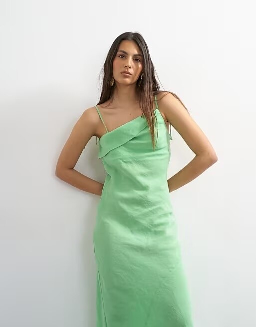 Model wearing an apple green satin slip bridesmaid dress with thin straps and midi length.