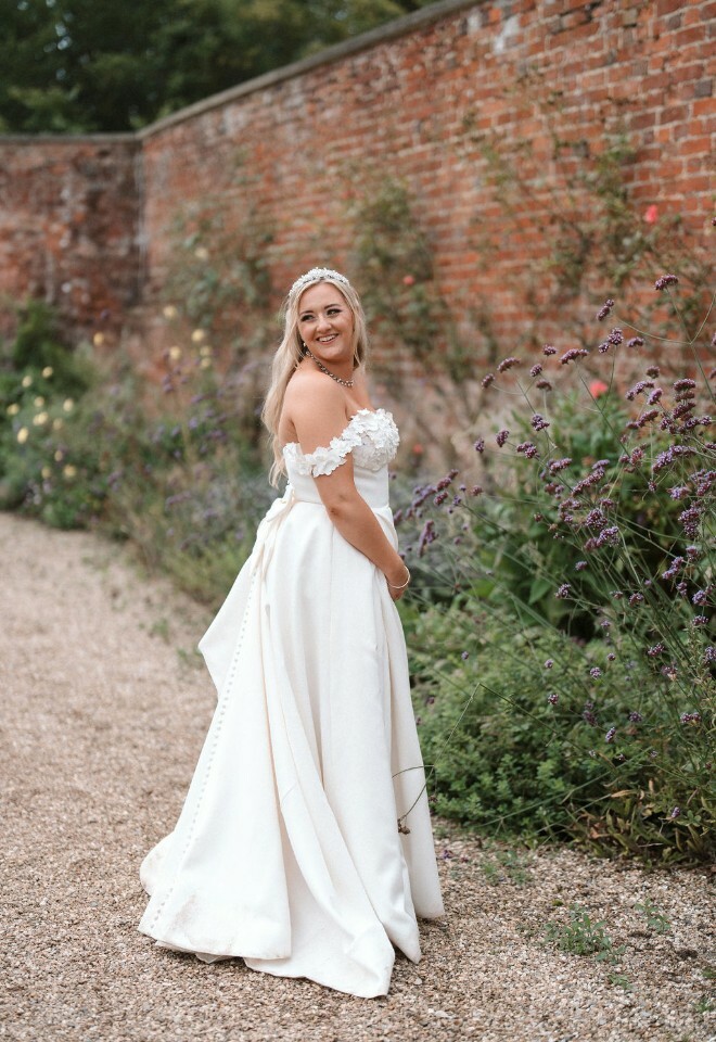 Bride, wears Justin Alexander a-line gown with 3d patterned bodice andposes in the gardens of Elmhay Park