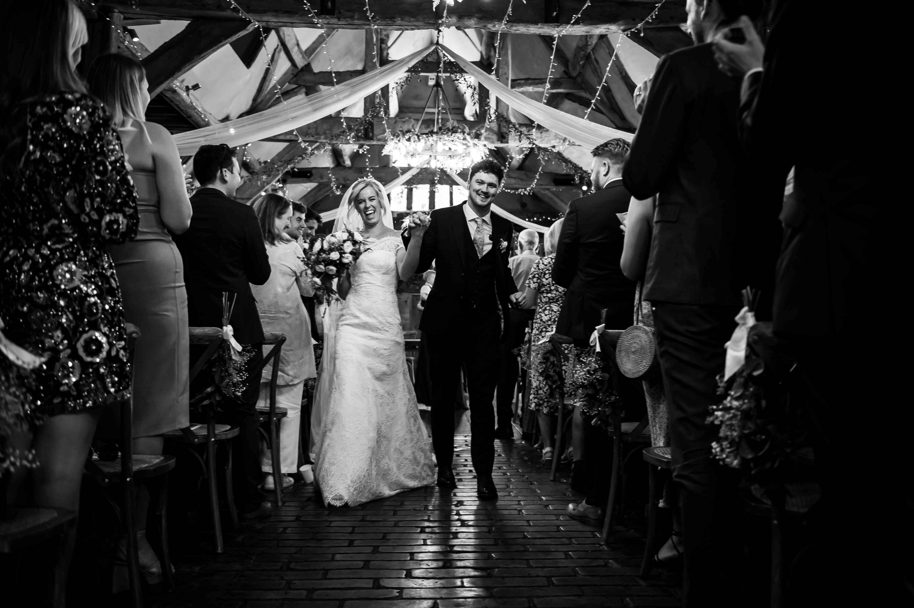 Newlyweds walking back down the aisle together in a black and white, photographed by Matthew Pattimore Photography, Oxfordshire