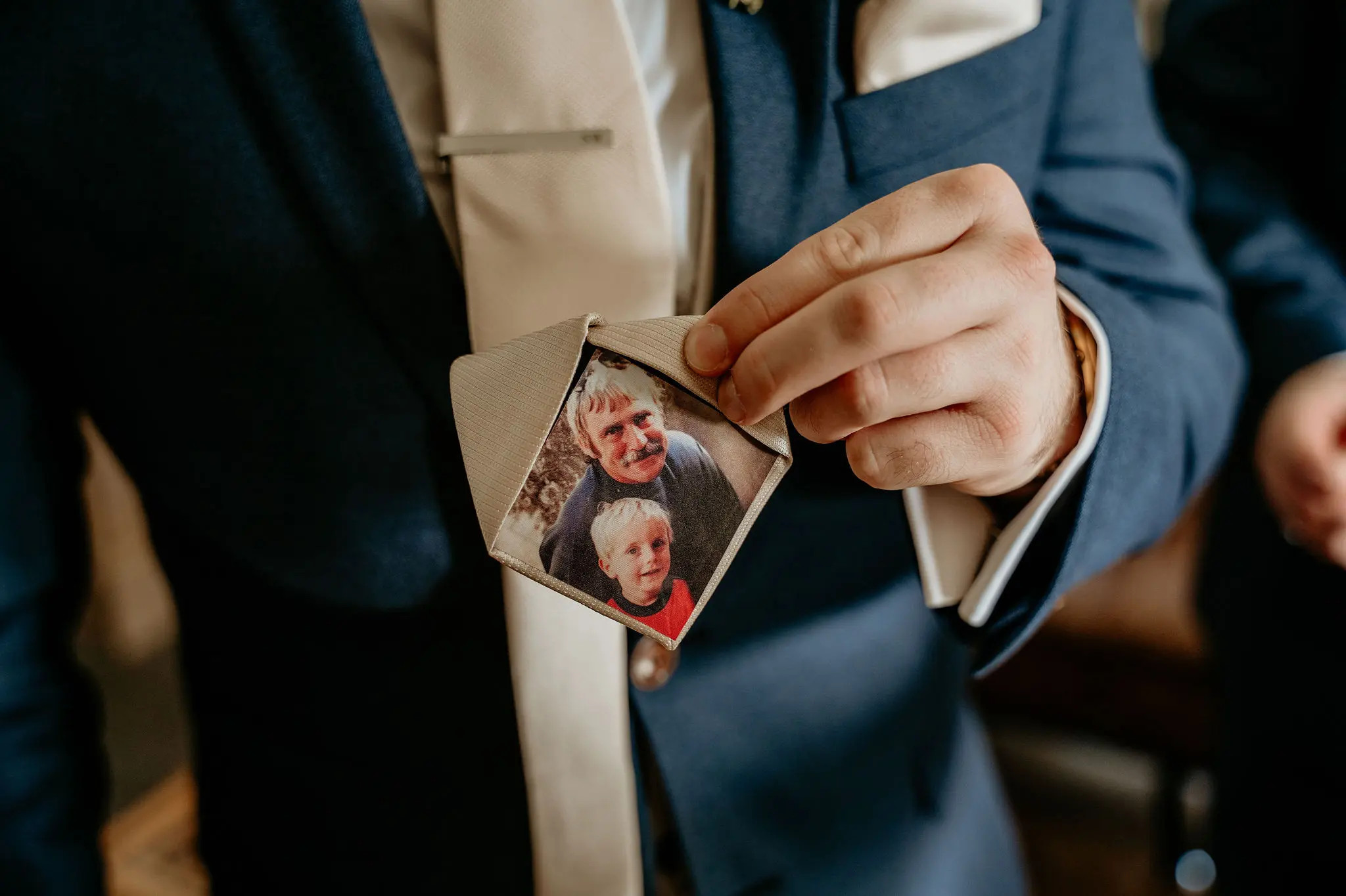 Groom holding a photograph of a loved one who has passed away inside his wedding tie.