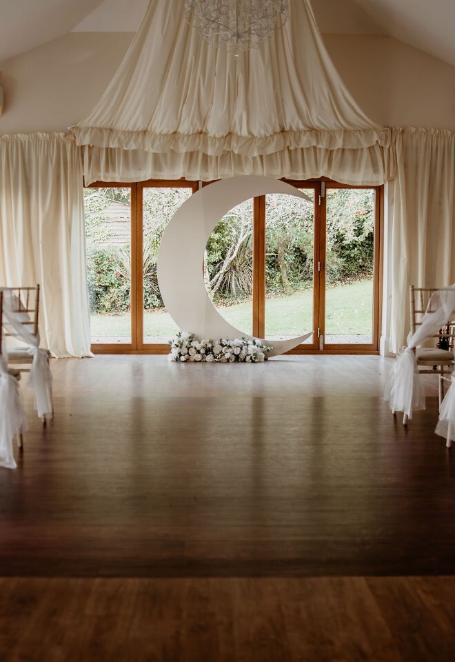 Indoor ceremony setup with aisle chairs and a large crescent moon backdrop