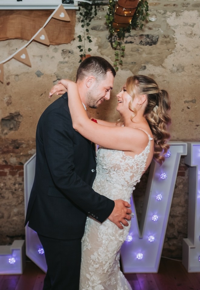 Rosie and Kyle standing close together in front of a lit up LOVE sign