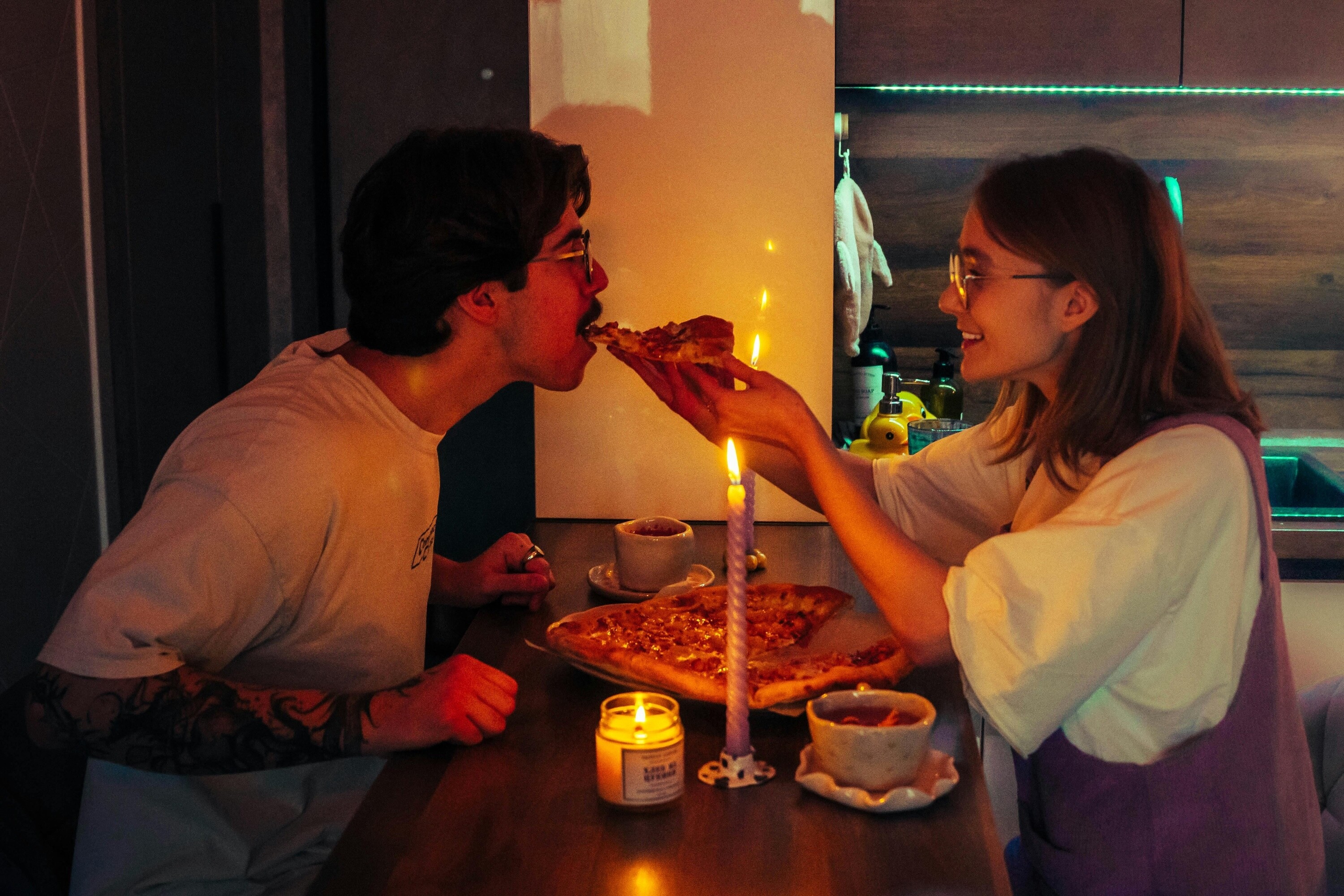 Couple enjoying a cosy date night at home with pizza and candlelight in the kitchen.