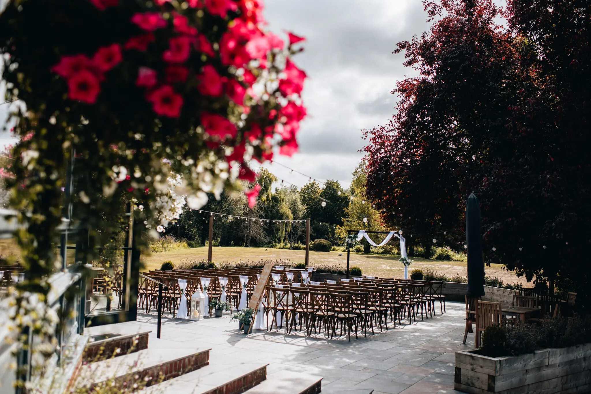Outdoor wedding ceremony setup on the terrace at The Old Mill Aldermaston in Berkshire, with wooden chairs, floral arch and countryside views.