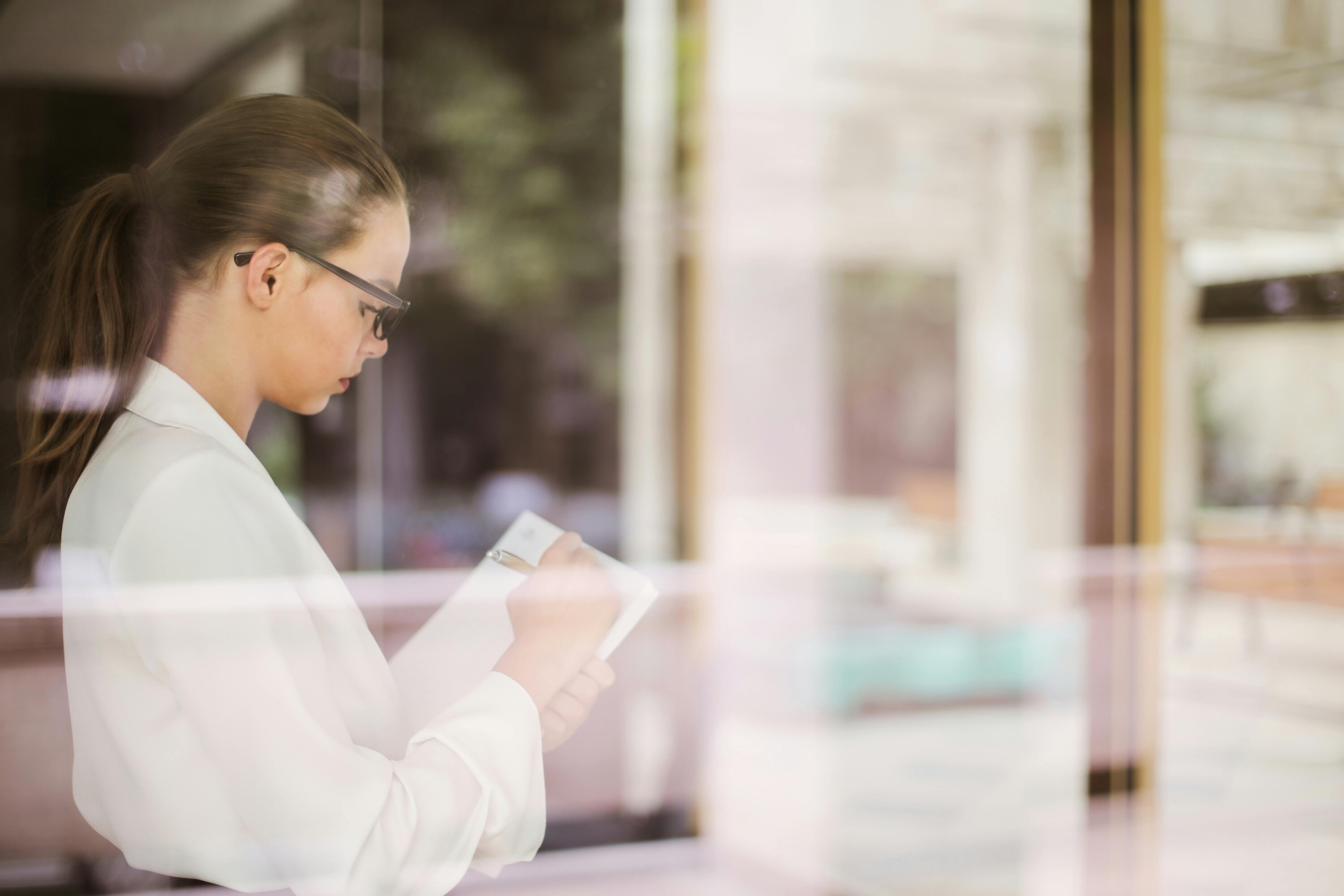 Woman photographed through a window. She is a weddin planner and writing something on a clipboard