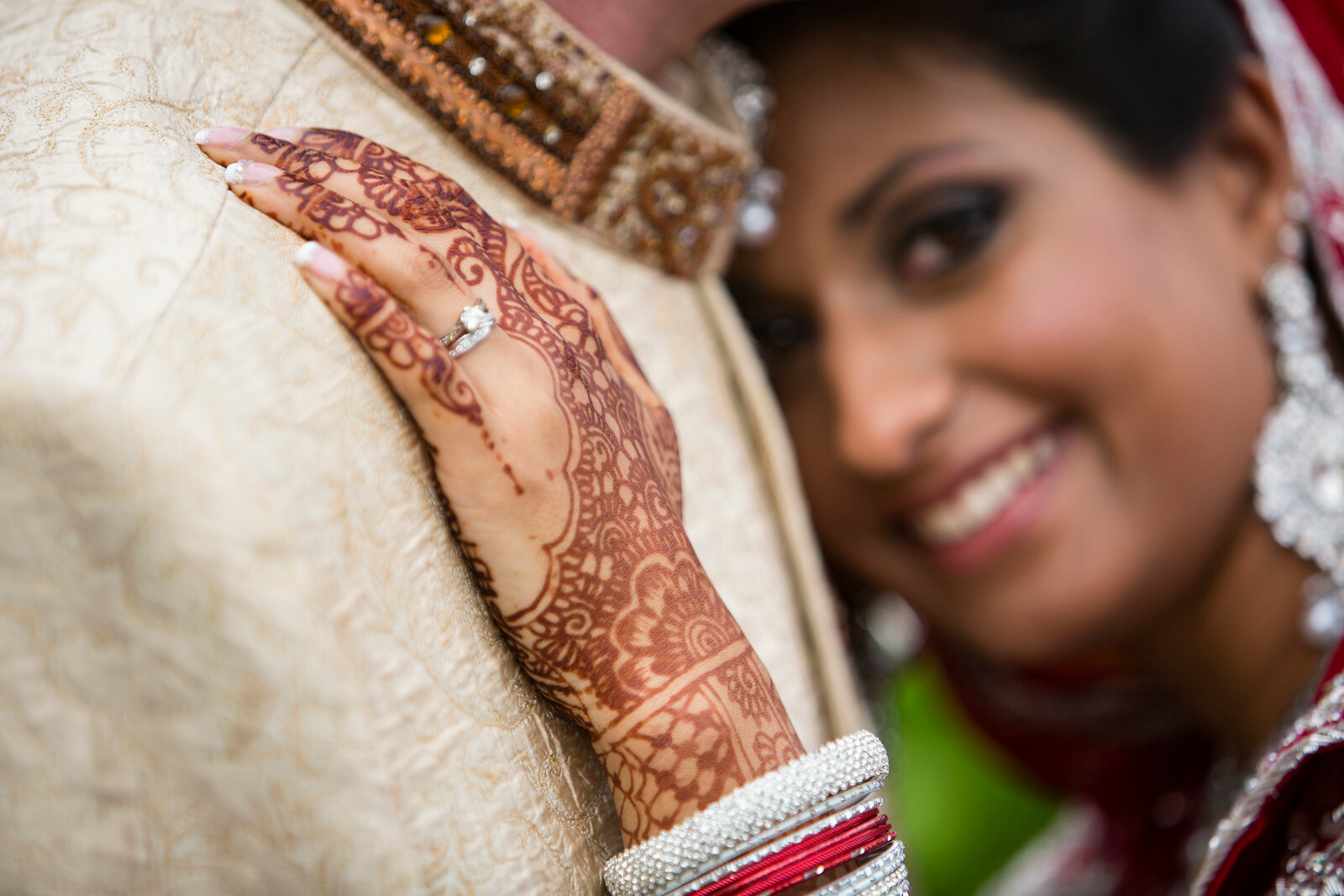 Close-up of a bride’s hand decorated with henna and wearing an engagement ring, with the bride slightly blurred in the background. Captured by Rob Wheal Photography, Oxfordshire.