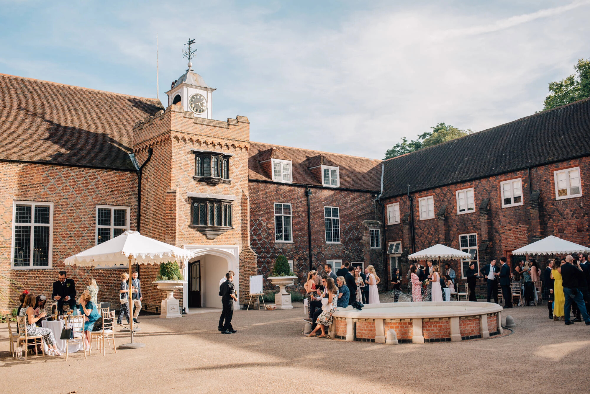 Wedding guests stand mingling in courtyard of Fulham Palace