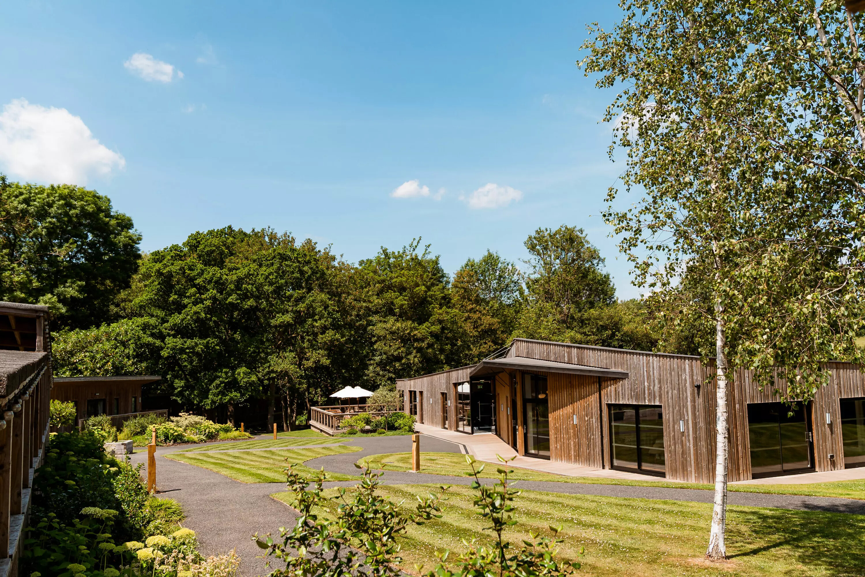 The Woodlands at Hothorpe in Leicestershire, featuring contemporary timber lodges, landscaped grounds and woodland surroundings under blue skies.