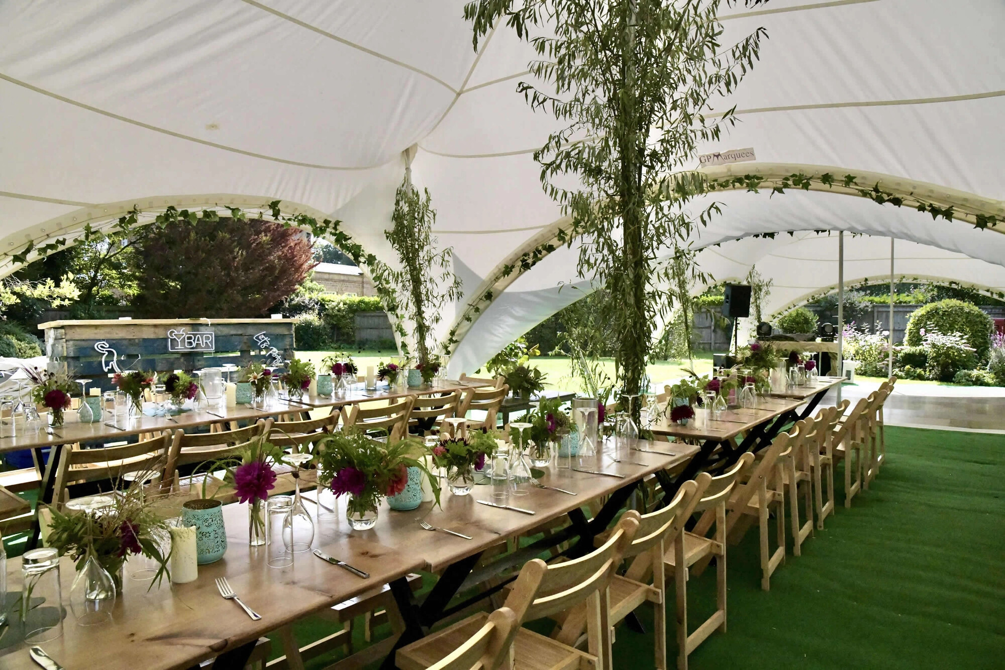 Wedding marquee reception with long banquet tables and open garden views by GP Marquees.