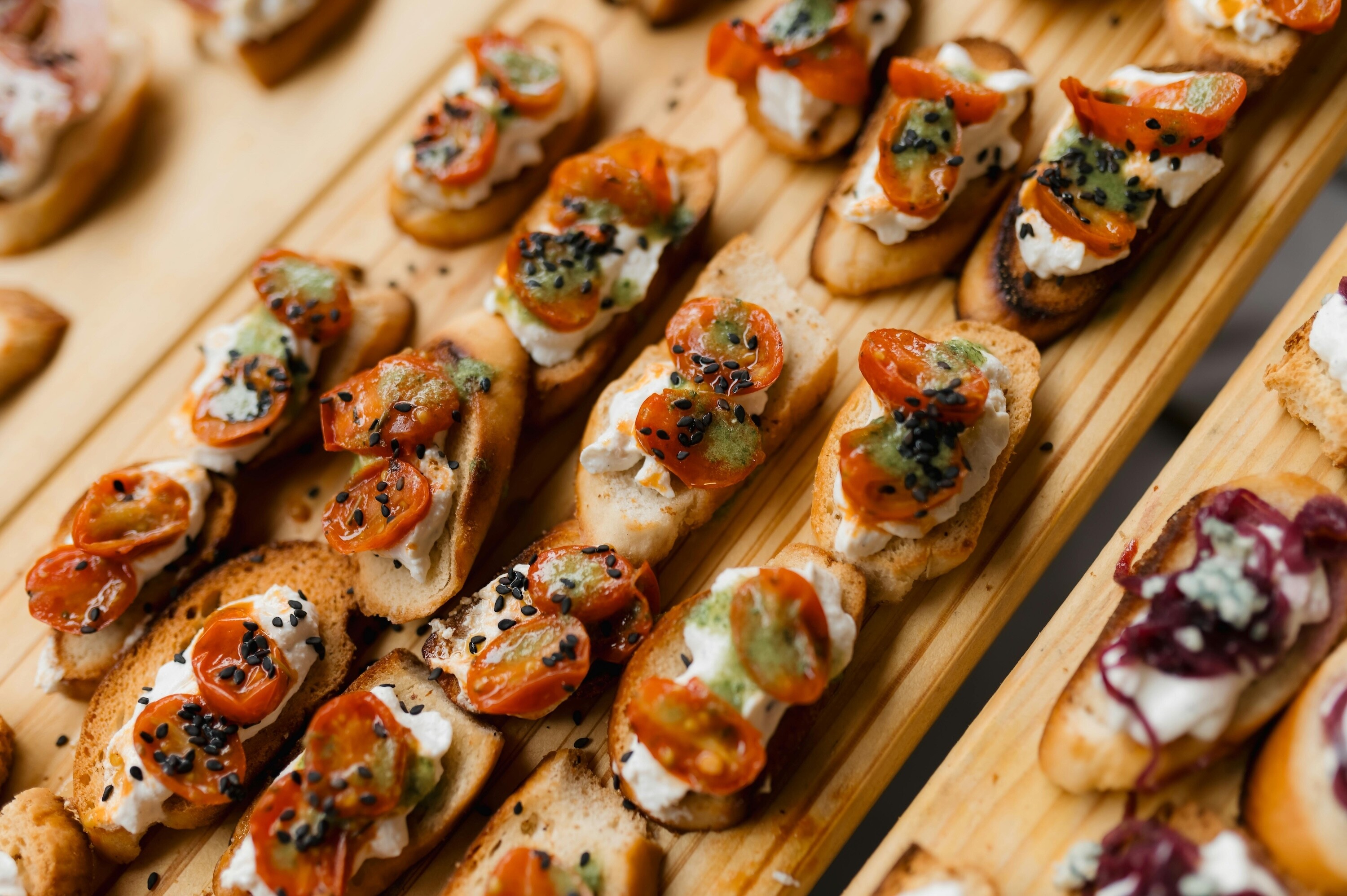 Sustainable wedding catering canapés served on reusable wooden platters, featuring seasonal tomato bruschetta with soft cheese and herbs.