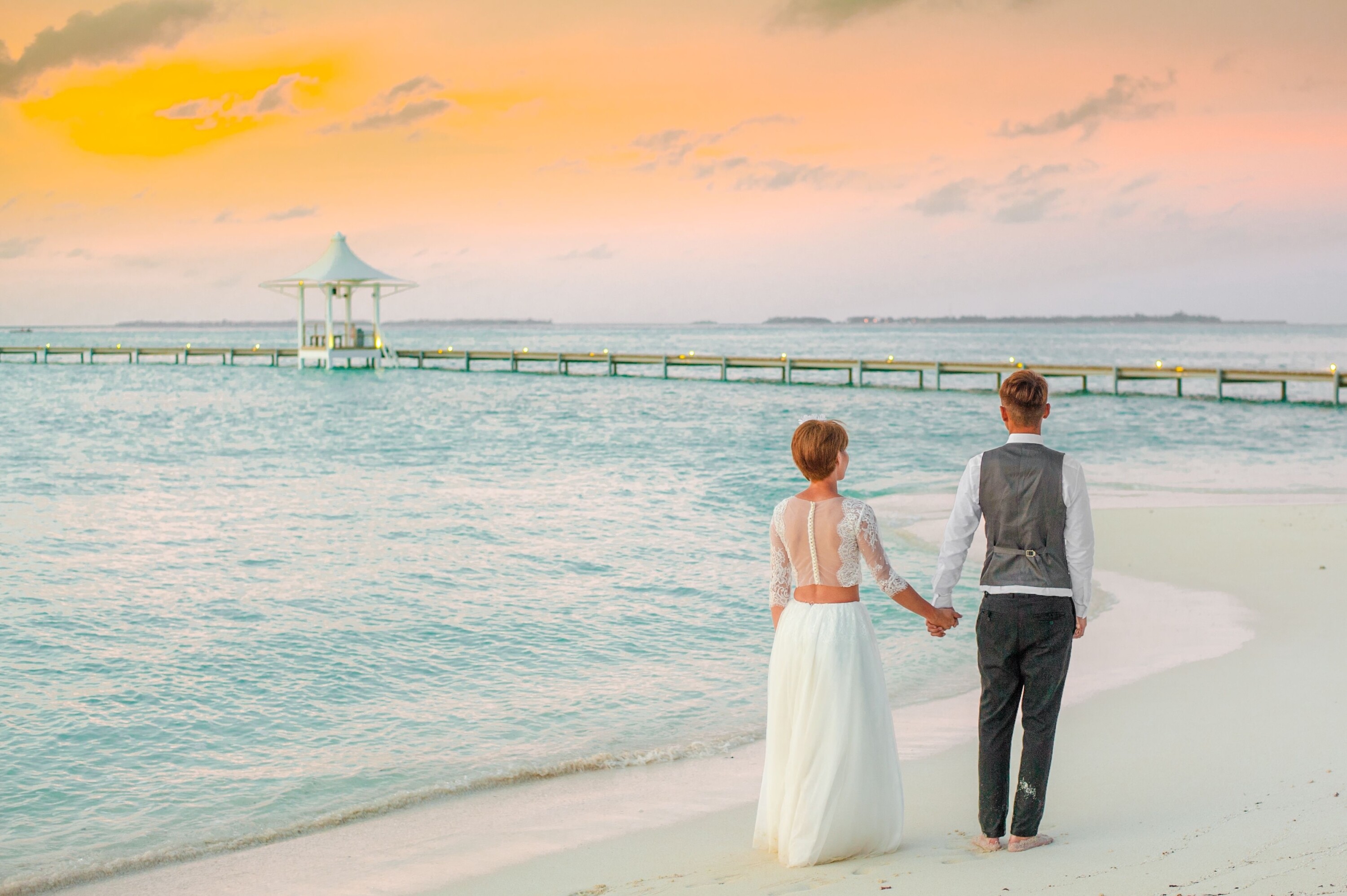 Bride and groom walk on the beach hand in hand