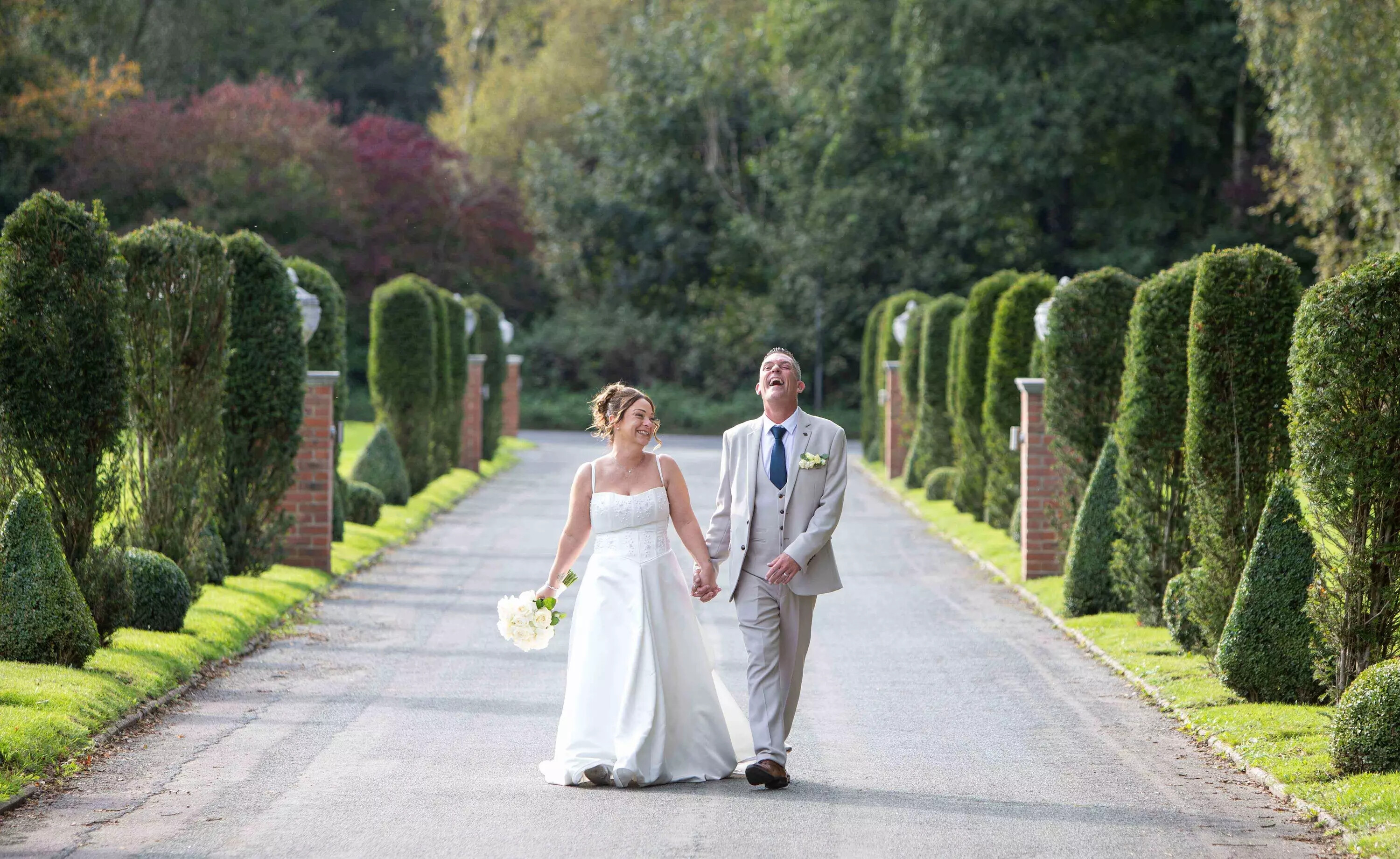 Wedding couple walking through road lined with hedges, photographed by Tony Graham Photography, West Sussex
