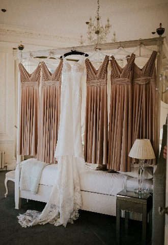 Bride and bridesmaid dresses hanging on four poster bed at Hedsor House wedding venue Buckinghamshire