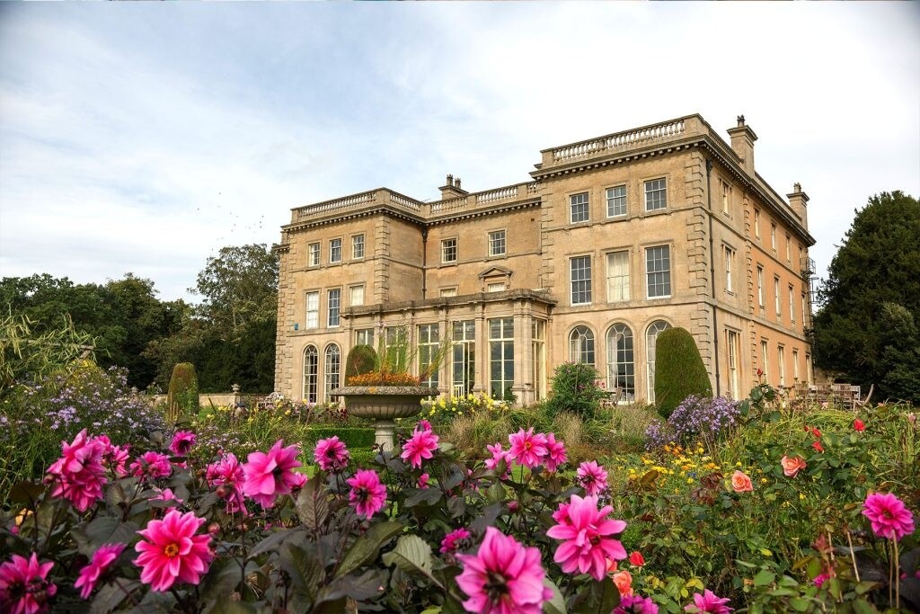 Exterior of Prestwold Hall in Leicestershire, with formal gardens, pink flowers in bloom and the historic country house behind.
