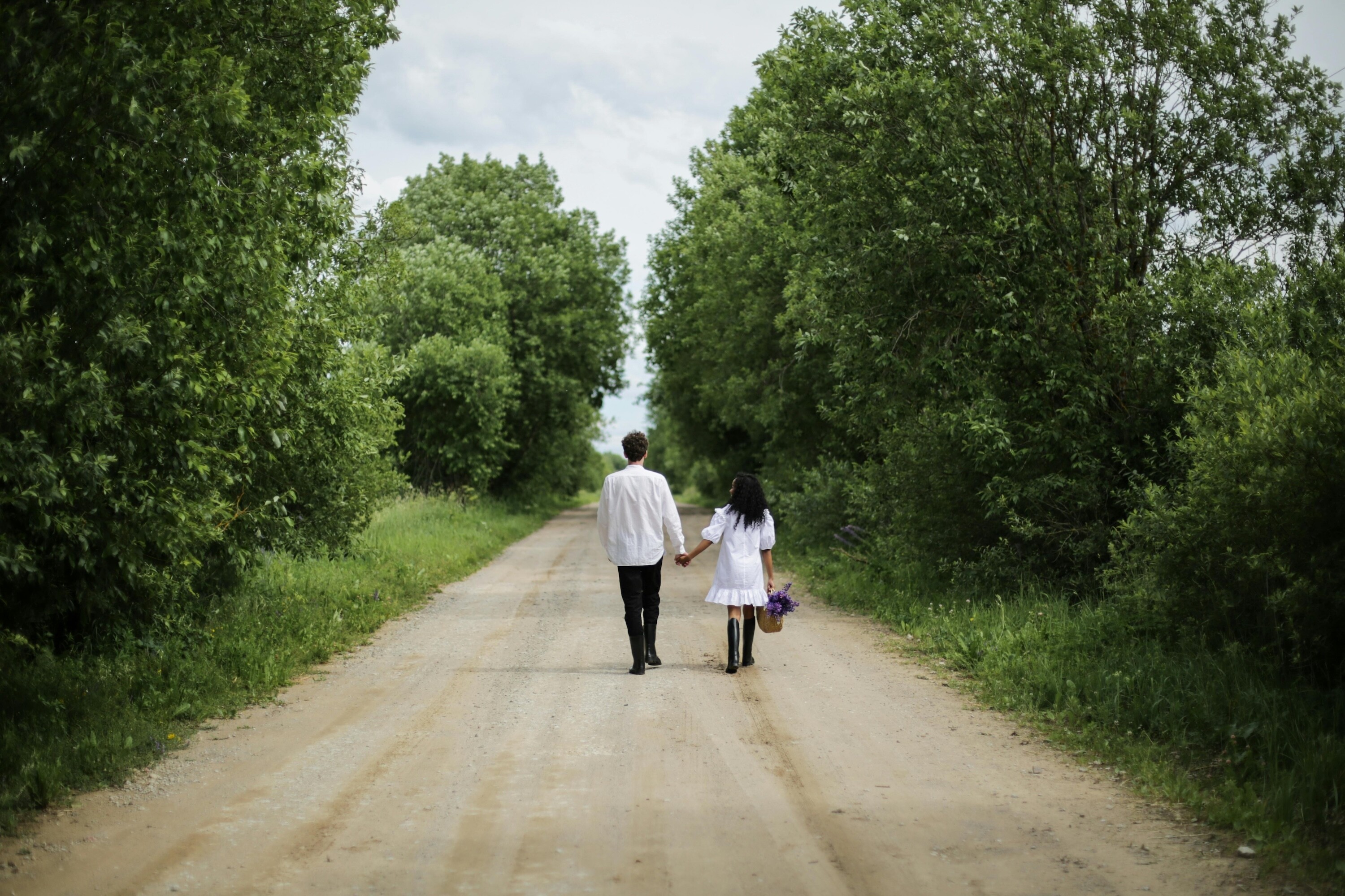 Couple walking hand in hand along a quiet countryside road surrounded by trees