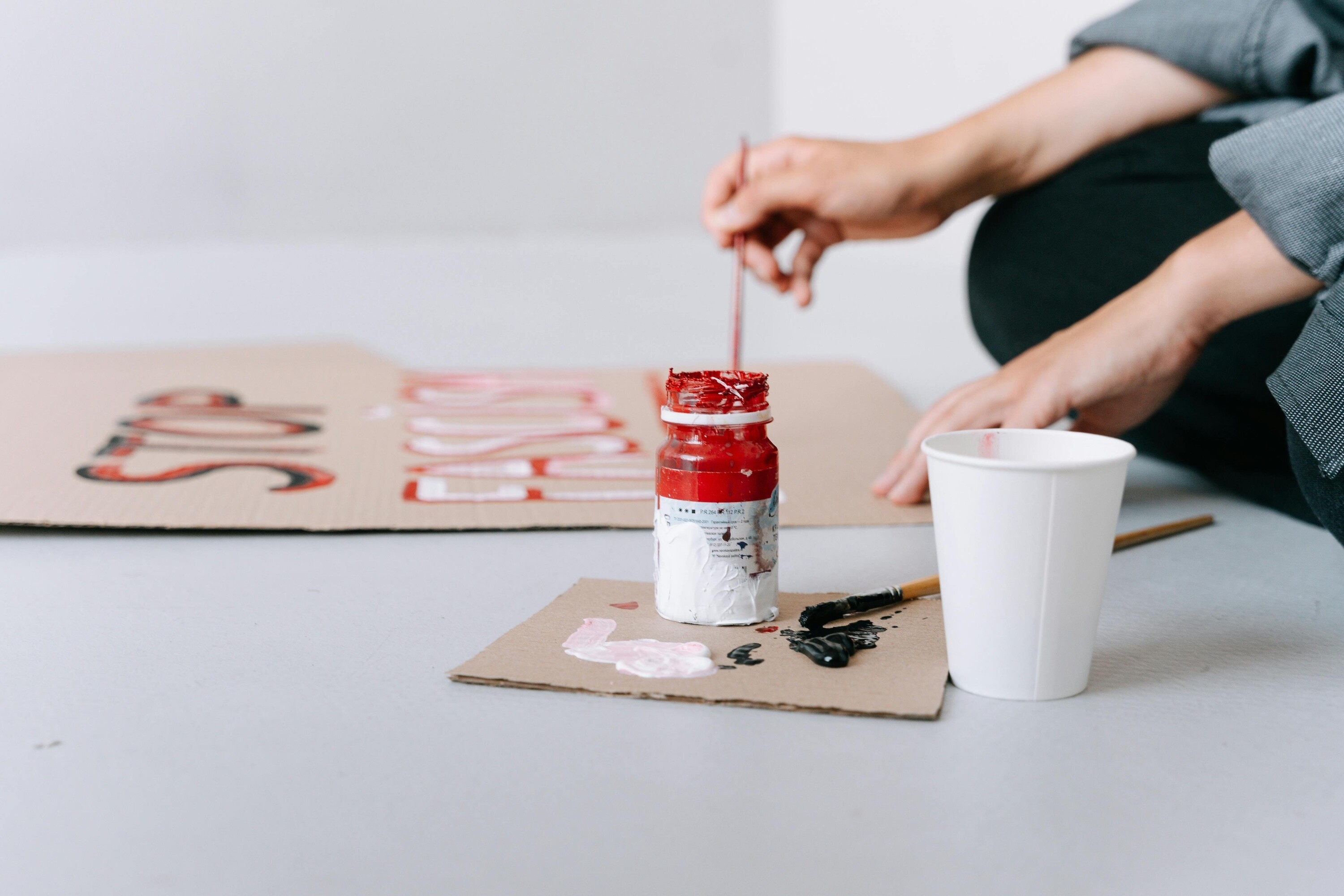Person painting a creative project at home with brushes, paint and cardboard materials.