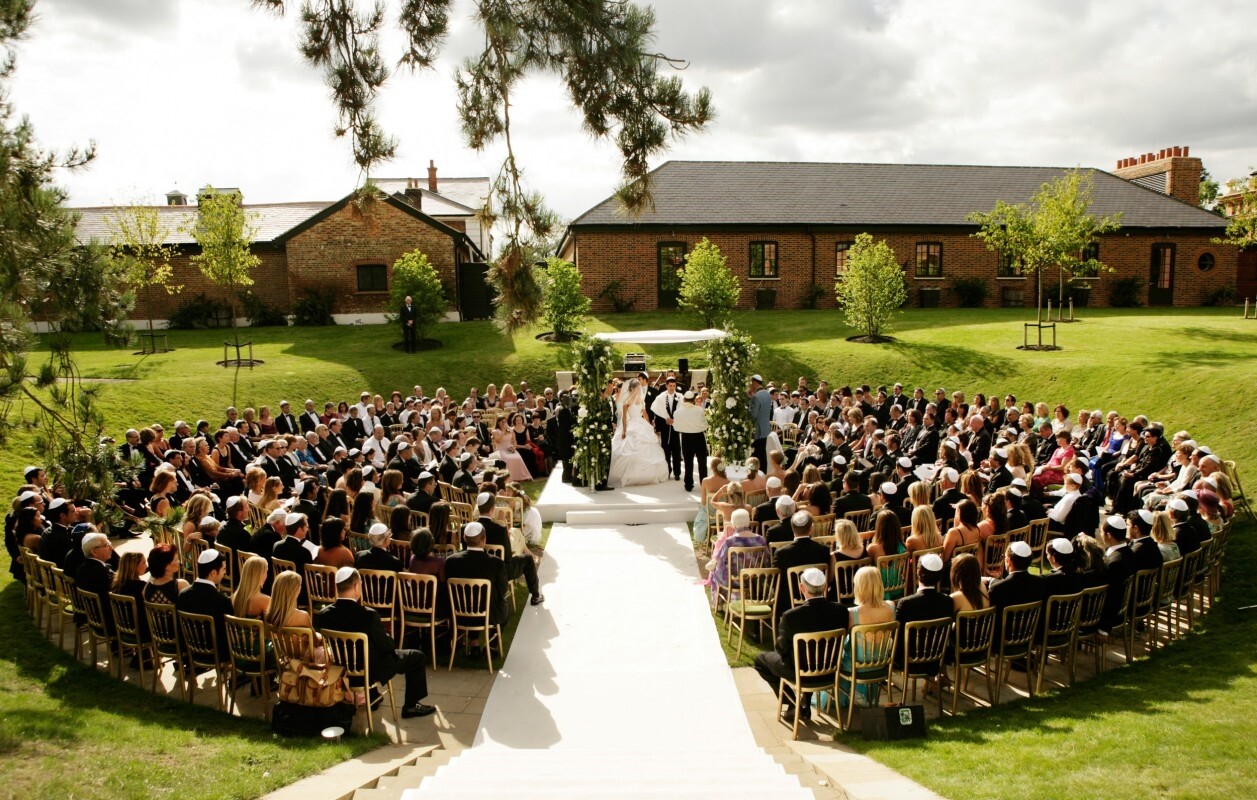 Outdoor wedding ceremony at The Grove in Watford, with guests seated around a central aisle in landscaped grounds
