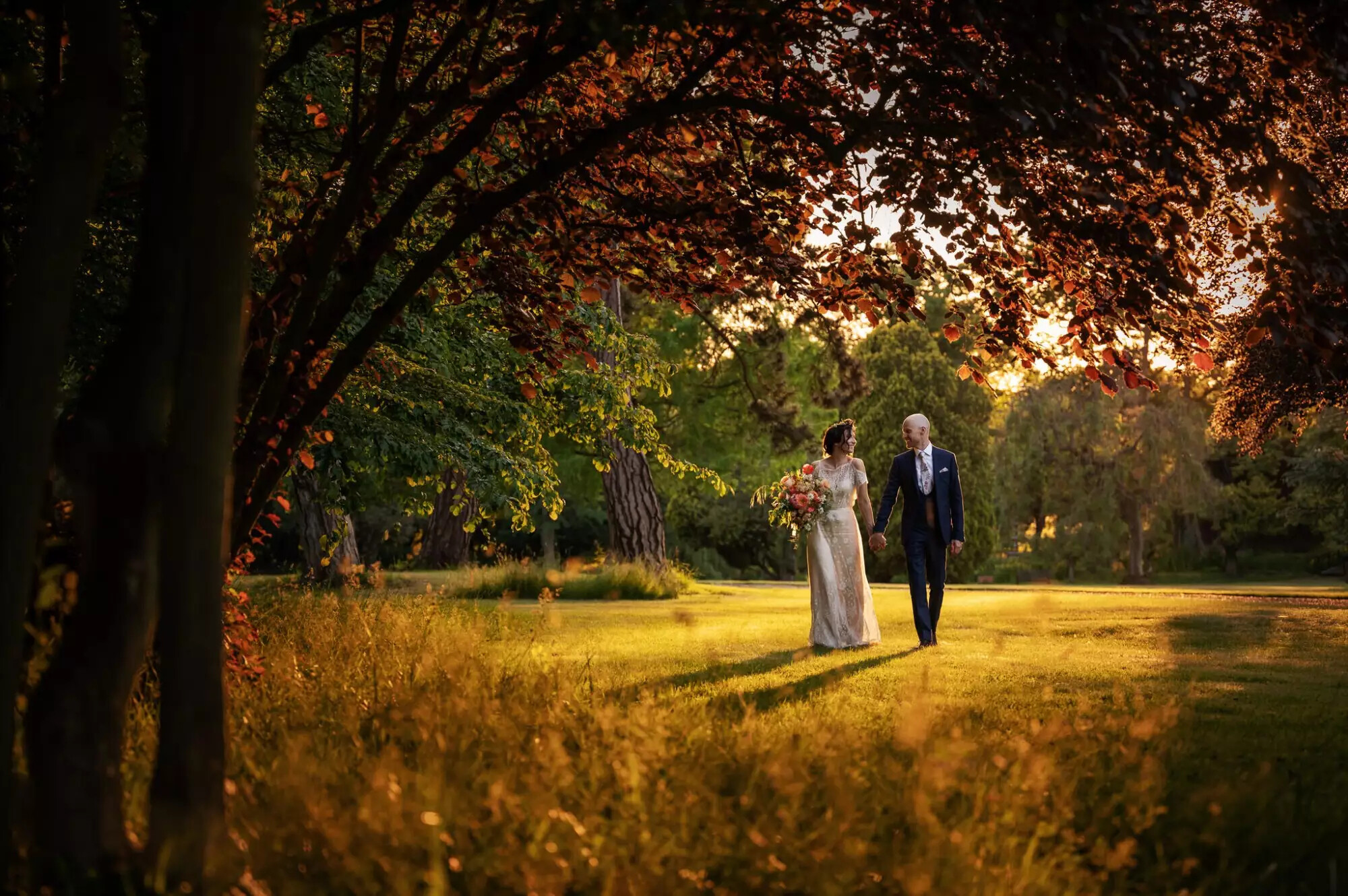Wedding couple walking through the grounds at Fanhams Hall with autumnal trees. Taken by Andy Sidders Photography, Buckinghamshire