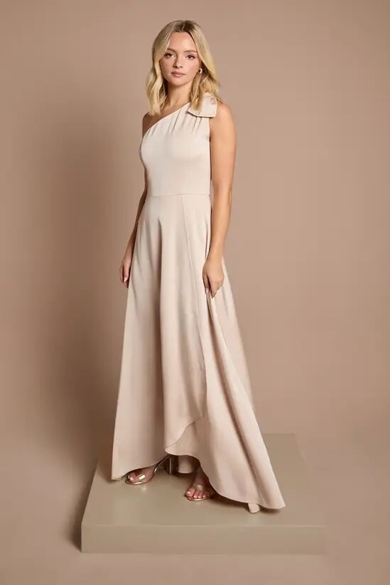 Teen bridesmaid wearing a champagne one shoulder bridesmaid dress with bow detail and flowing skirt.