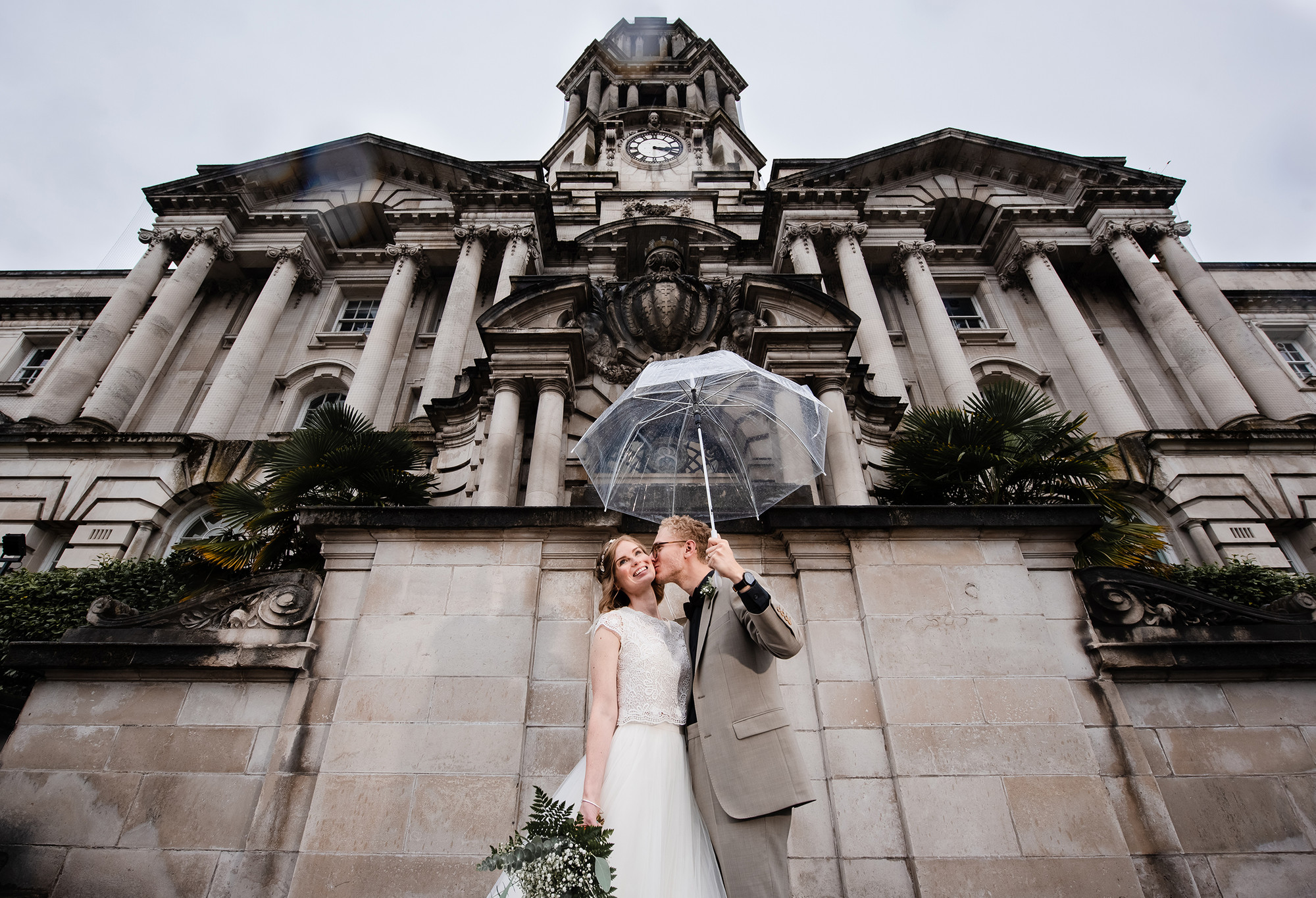 Bride and groom holding an umbrella outside of Stockport Town Hall