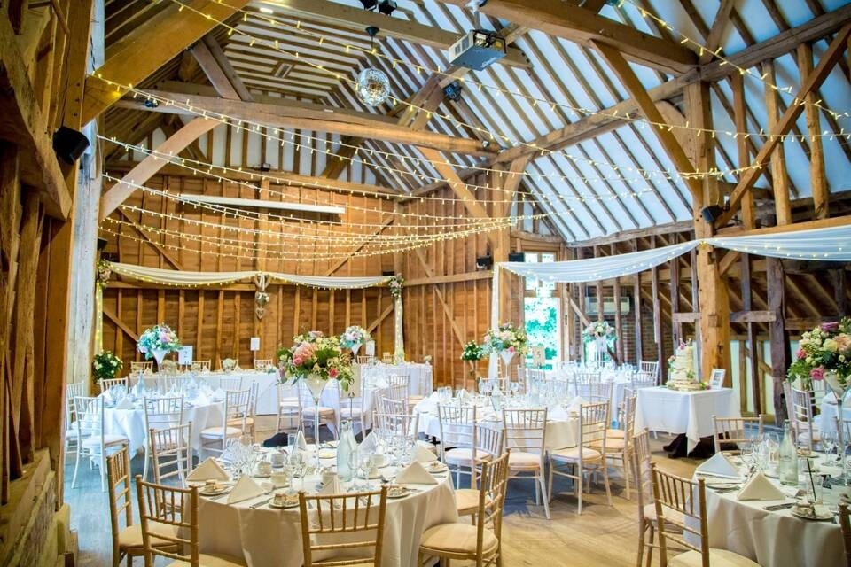 Rustic barn wedding reception at Tewin Bury Farm with exposed beams, fairy lights and round tables set for guests
