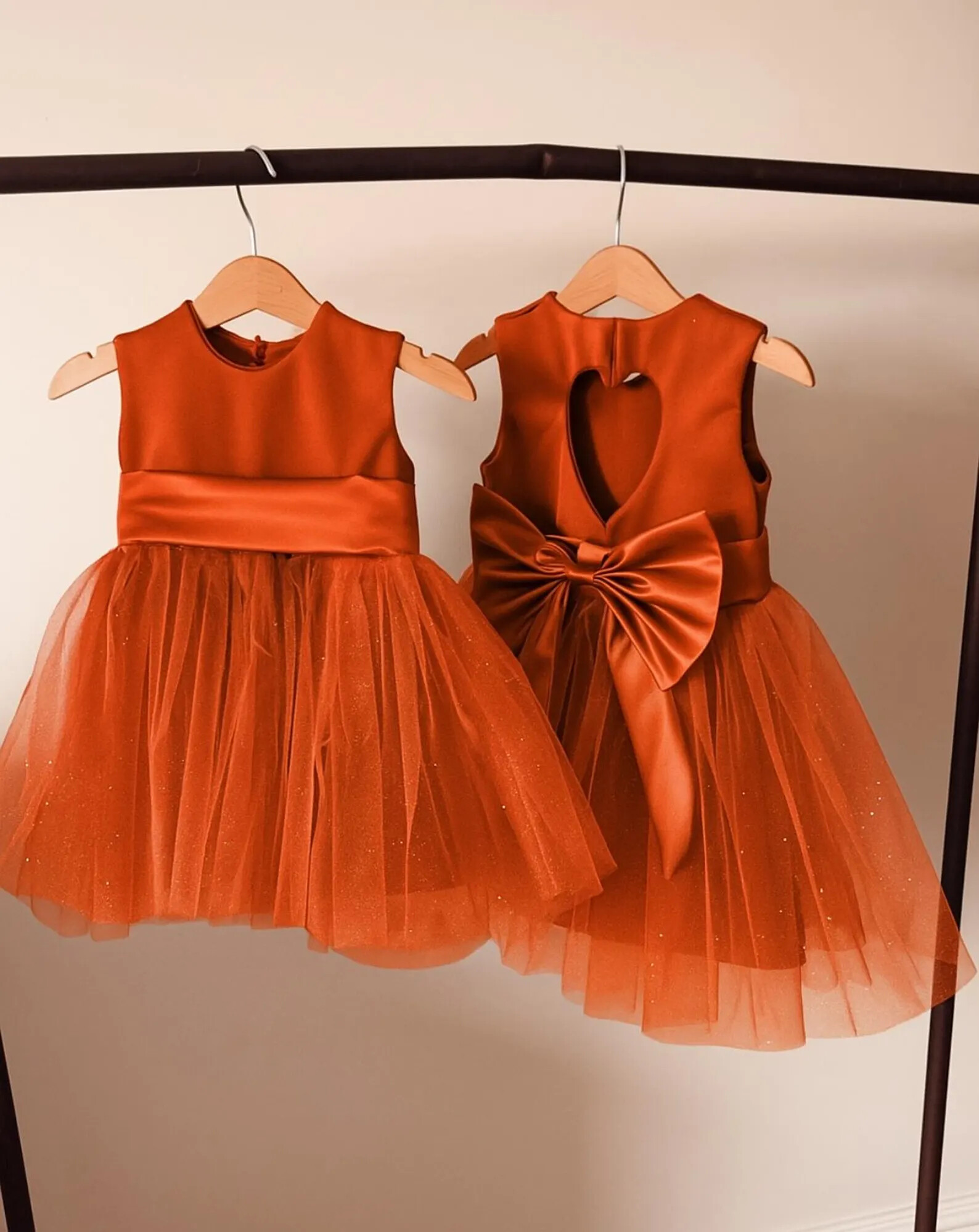 burnt orange flower girl dress with a big bow at the back on hangers