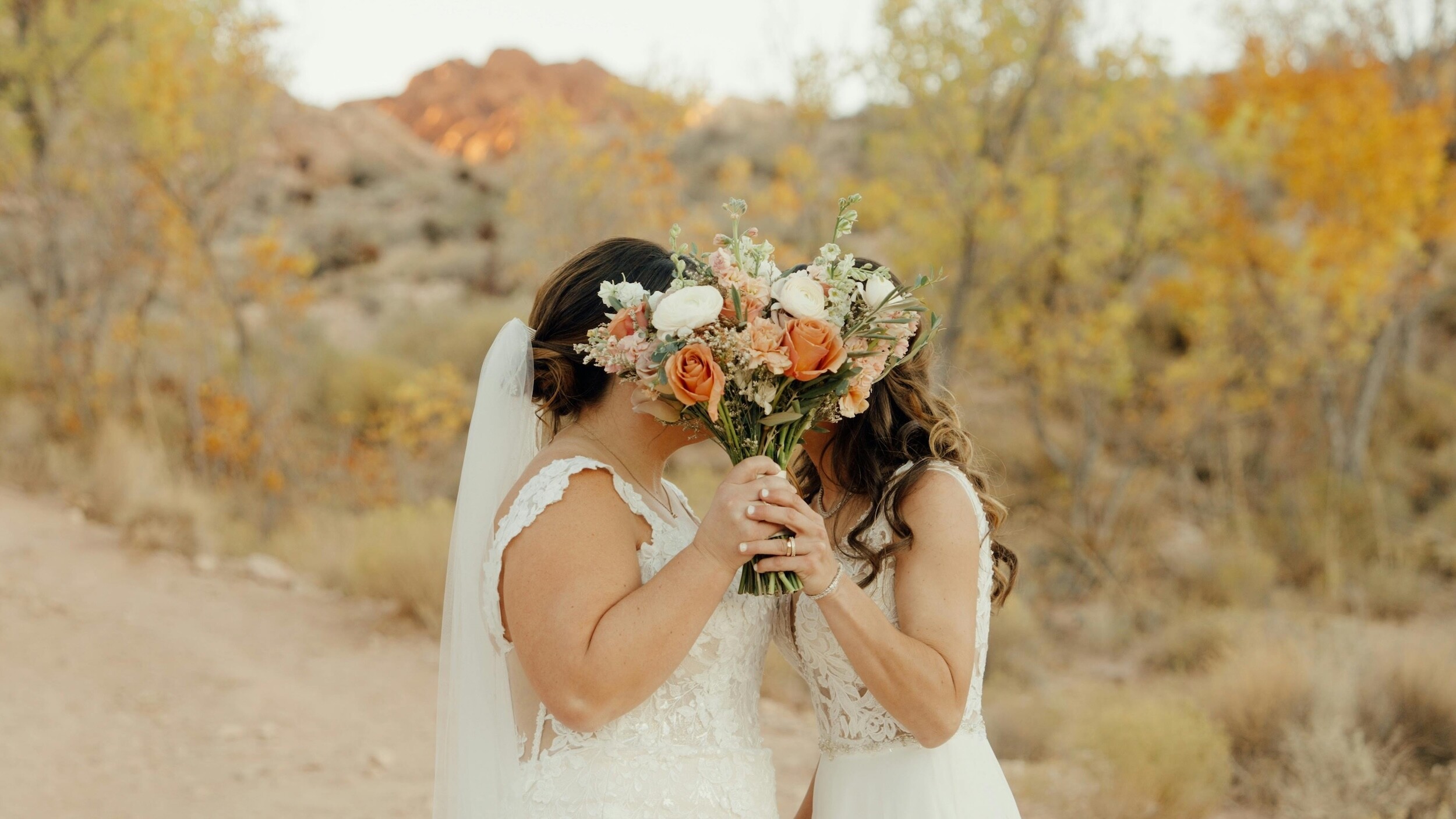 Brides hold a bouquet of flowers in front of their facts as they kiss on their wedding day