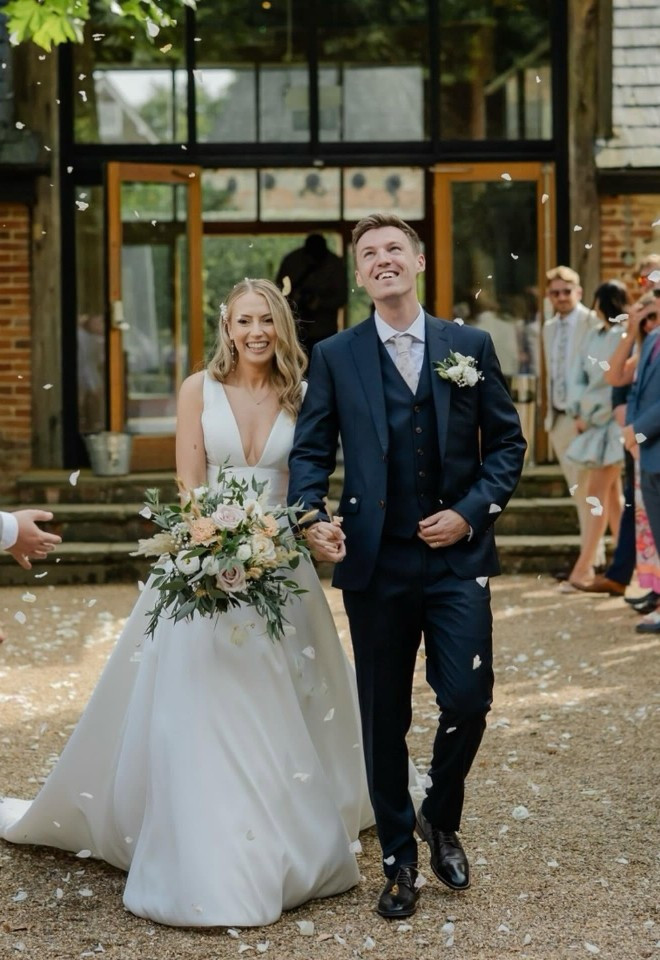 Our real bride wearing an Enzoani mikado A line with plunge neck walking hand in hand with the groom, from Little London Brides in Hampshire.