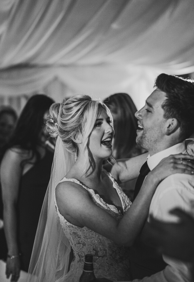 Bride and groom dancing together during lively wedding reception in black and white