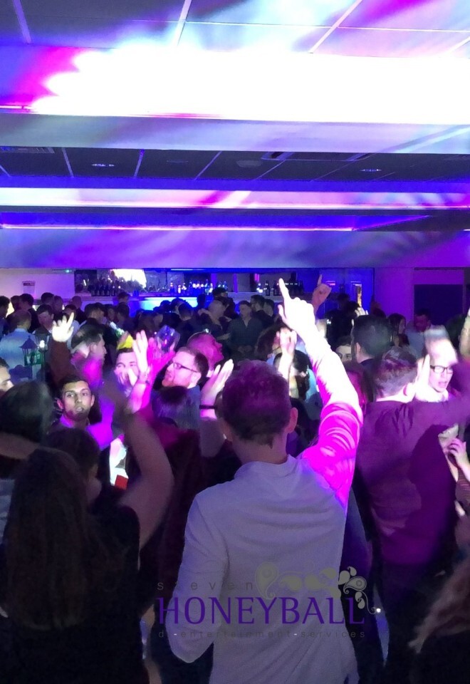 A crowded dance floor filled with people celebrating a wedding under vibrant purple, pink, and blue party lights.