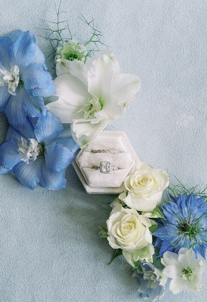 A silver vintage womens wedding and engagement ring with a cushion cut, surrounded by blue wedding flowers