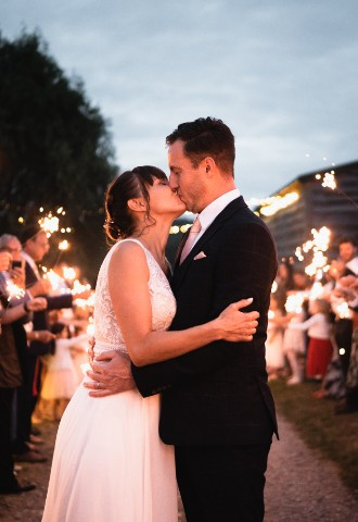 A bride and groom embrace and kiss as their guests surround them holding lot sparklers in the air